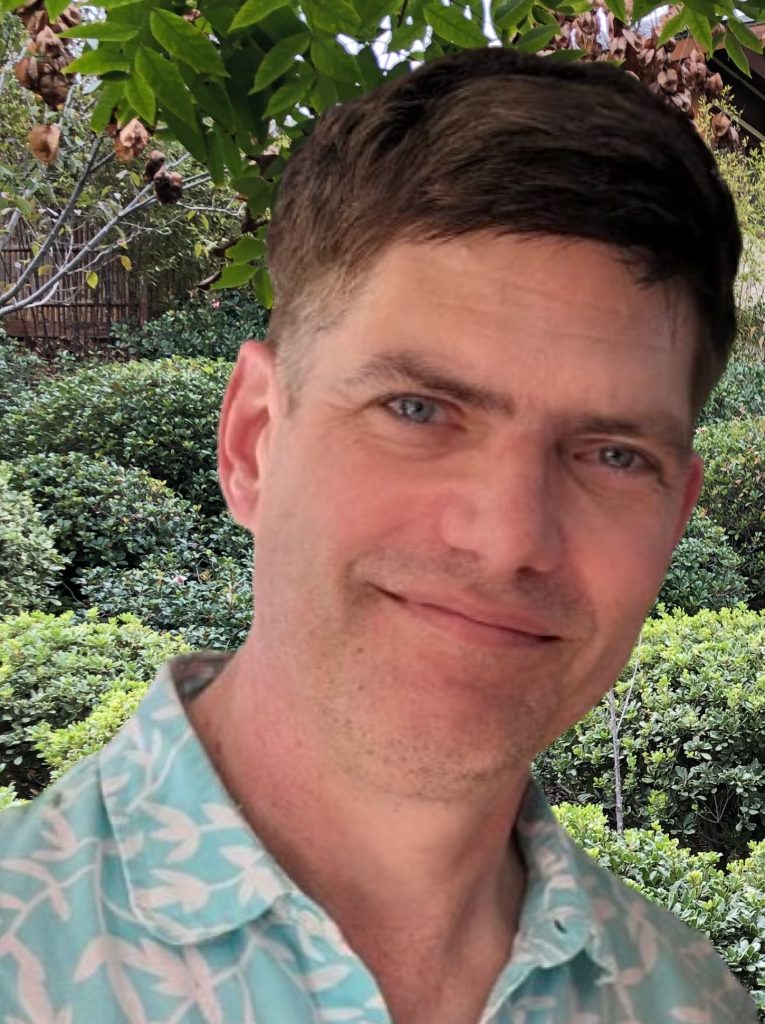 A man with a green shirt and brown hair smiles into the camera
